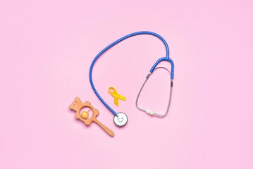 Fototapeta premium Golden awareness ribbon, rattle and stethoscope on color background. International Childhood Cancer Day