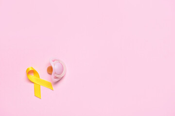 Golden awareness ribbon and pacifier on color background. International Childhood Cancer Day