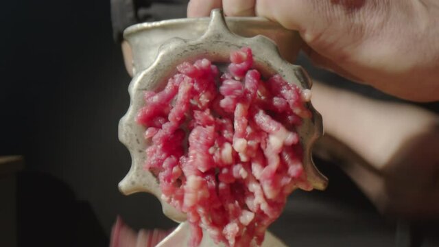 Zoom in shot of ground beef coming out from manual meat grinder operated by male chef