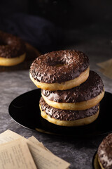 Chocolate donuts with a central hole, neatly placed on a black dish with a moody setting.