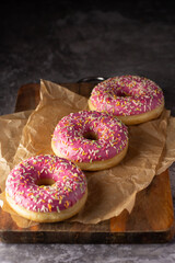 Close-up of pink glazed donuts with multicolored sprinkles on brown parchment, set on a wooden...