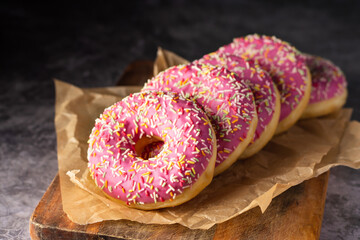 Three delicious donuts with pink frosting and colorful toppings, presented on crumpled paper and a wooden surface. - obrazy, fototapety, plakaty