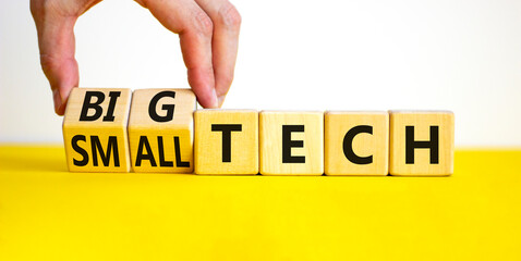 Big or small tech symbol. Businessman turns wooden cubes and changes concept words small tech to big tech. Beautiful yellow table white background, copy space. Business and big or small tech concept.