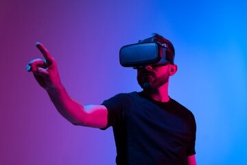 Bearded young man in virtual reality glasses in the studio with blue and pink light.