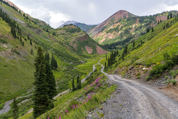 Fototapeta na wymiar Hidden Valley - A stormy Summer day view of a rugged steep backcountry road diving into a remote green mountain valley. Crested Butte, Colorado, USA. 