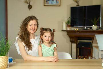 Portrait happy smile family. Mom and daughter at table look at cameras. two sisters laugh At home room and laugh. Place for text. childhood. Caucasian woman and girl in frame. Nanny child Babysitter.