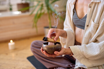 cropped woman sitting in lotus position with wooden stick and bowl meditating, relaxing....