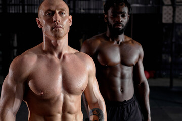 Fototapeta na wymiar Workout. Crossfit. Extreme. Training. Portrait of two interracial shirtless sportsmen before or after cross fit training, strong men with perfect body, abs muscles. focus on white caucasian bold guy