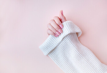 A woman's hand with a manicure in a white sweater on a pink background. Nude gel polish shade, top view, copy space.