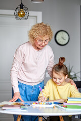 Creative activity. Caring aged grandma and preteen daughter friends sit at desk paint pictures in...