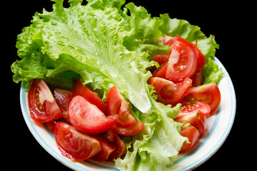 dish with tomatoes and lettuce with water drops frillis isolated on a black background