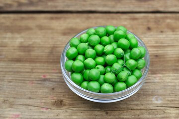 close up of young fresh green peas in a bowl on wooden table
