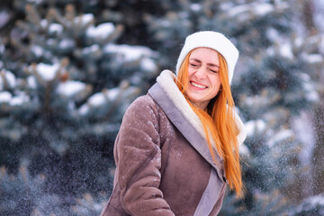 Winter ginger redhead girl throwing snowball at camera smiling happy having fun outdoors on snowing winter day playing in snow.