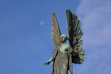 Angel statue at Parade Gardens in the city of Bath, Somerset. Moon and clouds next to woman angel wings