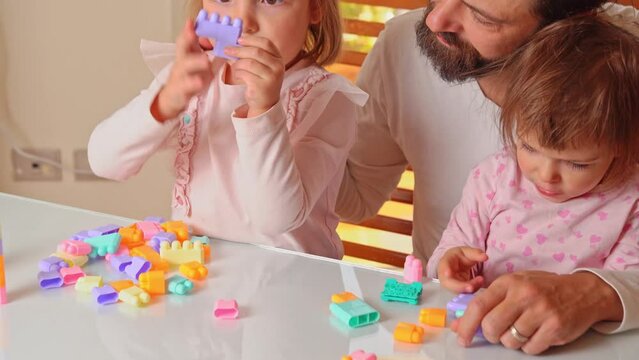 dad plays plastic constructor with his 2 daughters