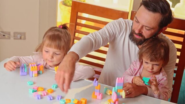 dad plays plastic constructor with his 2 daughters