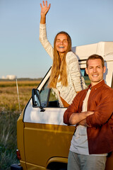 Adventurous soul. young smiling woman leaning out the van's window, enjoying the car travel. Man is...