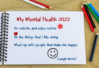 Mental health goals 2022 heading with list of ideas hand written in note book on desk. New year...