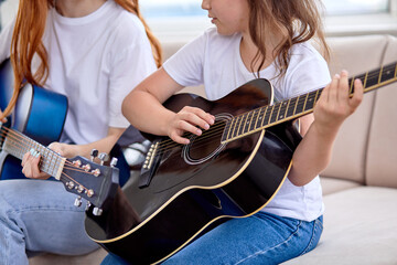 Close-up photo of kid girl hands playing acoustic guitar, sitting with teacher woman. music lesson...