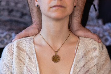 Close up and detailed view, on neck of a woman wearing a gold necklace with sacred geometry shri...