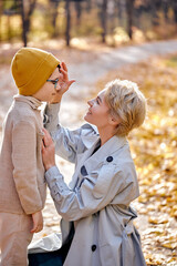 Mother and cute child boy feel love to each other, stand together in park or forest, hugging, talking. sunny day on autumn season. family, lifestyle, people, leisure, love concept