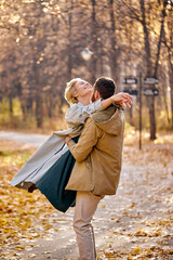 Couple walking and hugging in autumn forest, enjoy spending time together, cute caucasian man and woman in coats in love, outdoors, warm weather during leaf fall. carefree and happy. relationships