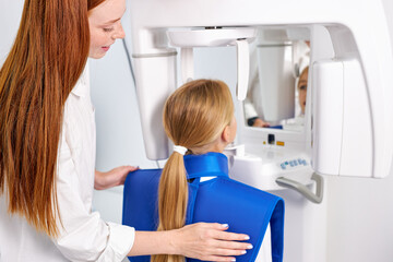 Woman dentist taking teeth x-ray of beautiful child patient using modern dental equipment. Young redhead caucasian female examining teeth in modern clinic, going to treat. Side view