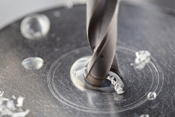 metal drill bit make holes in steel billet with tech oil on industrial drilling machine. Metal work...