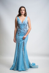 Fototapeta premium Full body portrait of gorgeous young brunette woman dressed in exquisite nude ball gown with lace top. Attractive female model in elegant strapless dress posing against white background.