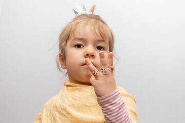 A little girl in a crown shows the rings on her hands, children's jewelry and bijouterie.