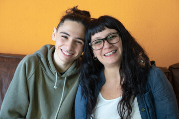 Portrait of a mother and her son looking at camera and being affectionate with orange background....