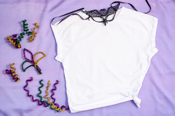 Mockup white t-shirt decorated carnival mask and glitter decor. Mardy Gras apparel flatlay on...