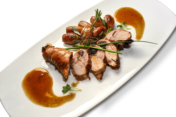 Baked rabbit roll stuffed with prunes, slices with potatoes and aromatic herbs on white plate isolated on white