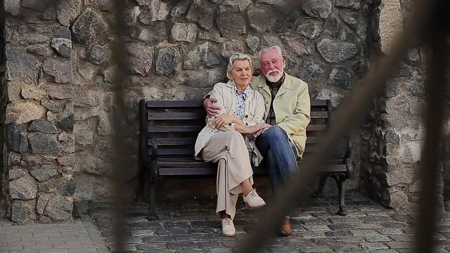 Man with woman sitting on bench in front of stone wall