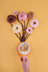 hand holding cup of coffee and various donuts on coffee beans like balloons on a yellow background