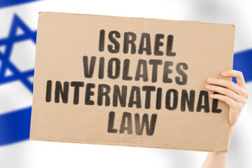 The phrase " Israel violates international law " on a banner in men's hand with blurred Israeli flag on the background. Political negotiations. Relationship. Illegal actions. Legislation. Conflict