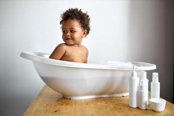 Happy laughing Infant black baby toddler taking bath with foam bubbles. Bathing and washing of...