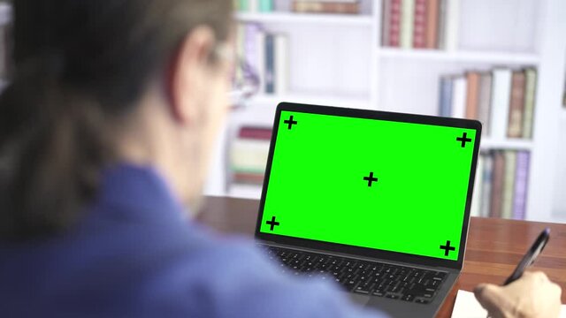Over the shoulder shot of a business man working looking at green screen. Office person using laptop computer with green screen.