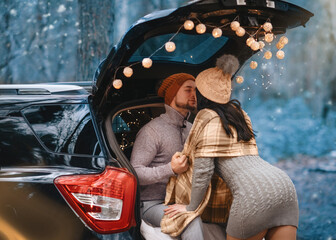 couple having date and sitting in car in winter clothes in snowing forest