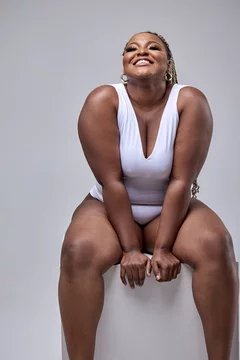 Cheerful fat black woman in white bodysuit on white background