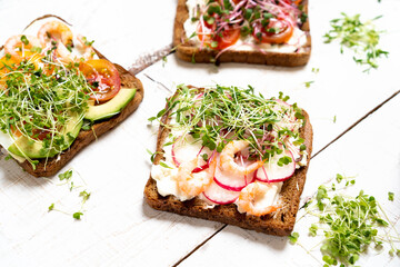 Varied breakfast, appetizer wholegrain bread sandwiches, toasters with cream cheese, radish, avocado, tomatoes, shrimp, egg, micro greens on a light background, top view, vertical photo
