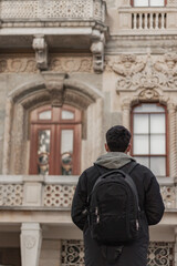 Back pose of young tourist boy wearing mask. He has back pack. He is looking to historical old building. The focus is on boy. Background is flu. Vertical photo.