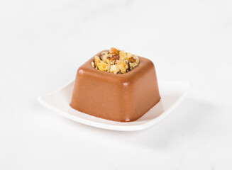 Chocolate nut cream dessert in the shape of a square savarin on a plate on a white background