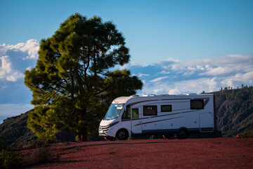 Holiday vacation and travel adventure concept lifestyle. Big motorhome camper van parked near a big tree and blue sky with mountains in background