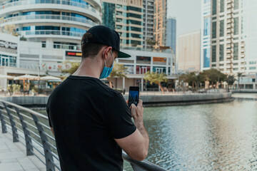 Person tourist with medical mask outdoor holding phone and taking pictures and videos of the city on the modern smartphone camera