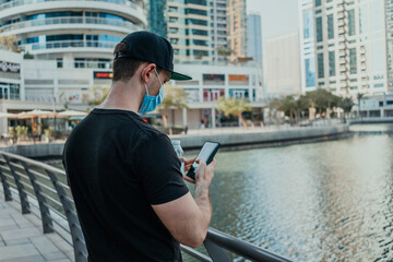 Person tourist with medical mask outdoor holding phone and taking pictures and videos of the city on the modern smartphone camera