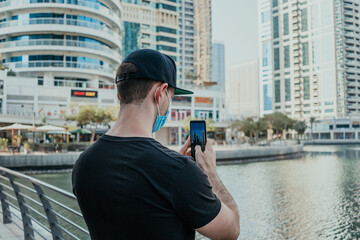 Person tourist with medical mask outdoor holding phone and taking pictures and videos of the city on the modern smartphone camera