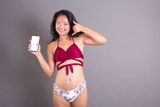 young chinese girl in bikini showing screen and call-me gesture