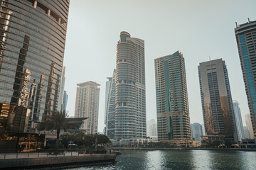 Fototapeta premium Modern city skyscrapers buildings at sunset time with business and residential towers around the lake and palm trees