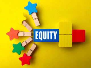 Top view colored wooden clips and wooden block with word EQUITY on yellow background.